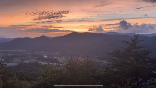 A scenic view of mountains at sunset, with vibrant colors in the sky and lush greenery in the foreground.