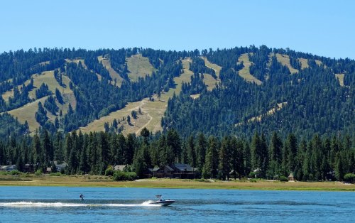 A scenic view of a lake with a person water skiing, surrounded by green hills and dense forests in the background.