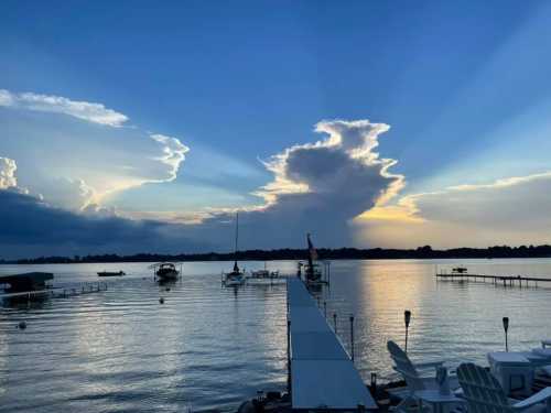 A serene lake at sunset, with boats docked and dramatic clouds casting rays of light across the water.