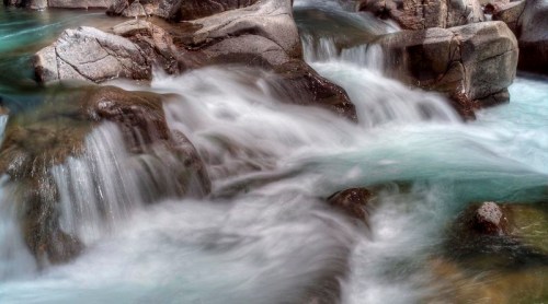A serene stream flows over smooth rocks, creating a tranquil scene with gentle water movement and soft colors.