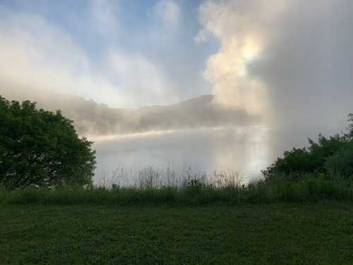 A serene lake surrounded by misty hills and lush greenery under a soft morning light.