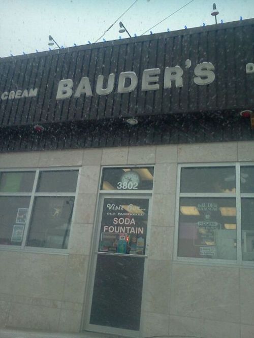 Sign for Bauder's Ice Cream with a storefront featuring a "Soda Fountain" entrance. Snow is visible in the foreground.