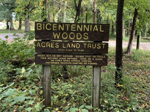 Sign for Bicentennial Woods, Acres Land Trust, with rules about trails, pets, and camping in a wooded area.