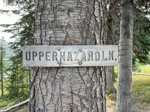 Wooden sign on a tree reading "UPPER HAZARD LK" in a forested area with trees in the background.