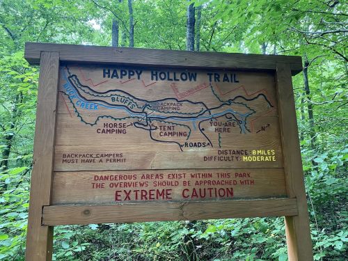 Trail sign for Happy Hollow Trail, featuring a map, distance, and warnings about dangerous areas.