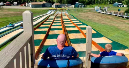 A man and a child sit on inflatable tubes at the top of a colorful water slide, ready to go down.