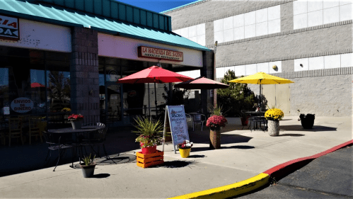 Outdoor seating area of a restaurant with colorful umbrellas, potted plants, and a sign advertising specials.