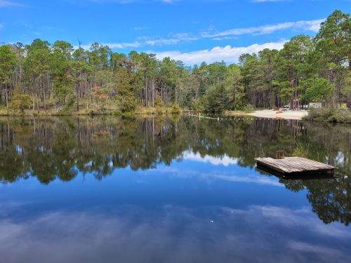 A serene lake surrounded by trees, reflecting the sky and a small dock in the foreground.