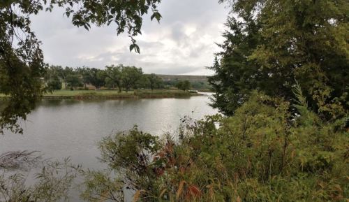 A serene river scene surrounded by lush greenery and trees under a cloudy sky.
