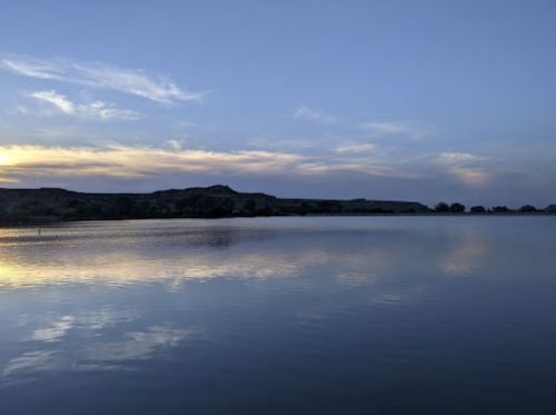 A serene lake at dusk, reflecting the sky and surrounding hills under a colorful sunset.