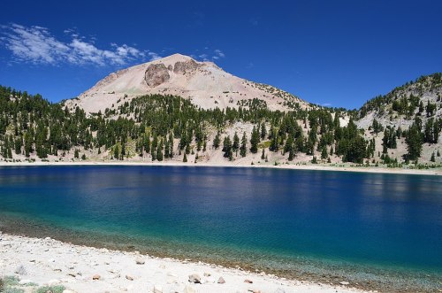 A serene lake surrounded by lush trees and a mountain under a clear blue sky.