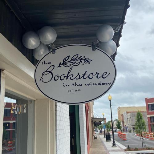 Sign for "the Bookstore in the Window," established 2019, hanging outside a storefront with decorative balloons.