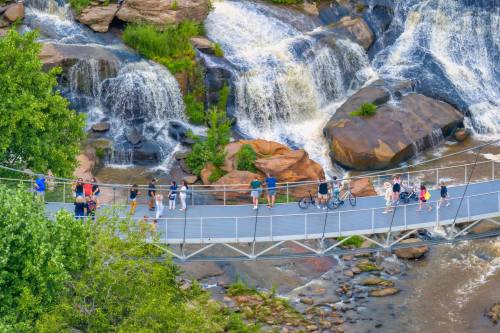 Aerial view of a bridge over a waterfall, with people walking, biking, and enjoying the scenic landscape.