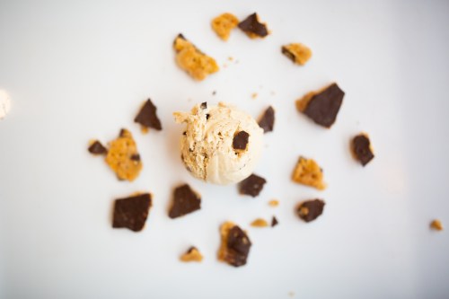 A scoop of ice cream surrounded by chocolate and cookie crumbles on a white plate.