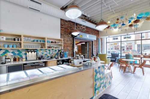Bright café interior featuring a colorful counter, coffee machines, and seating area with large windows.