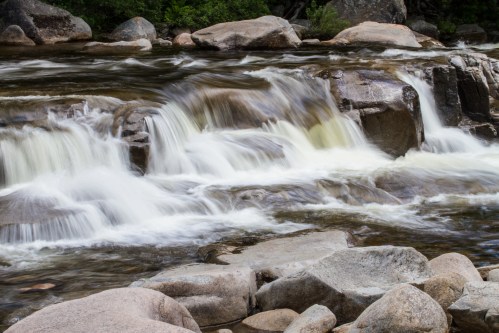 A serene river flows over smooth rocks, creating gentle waterfalls amidst lush greenery.