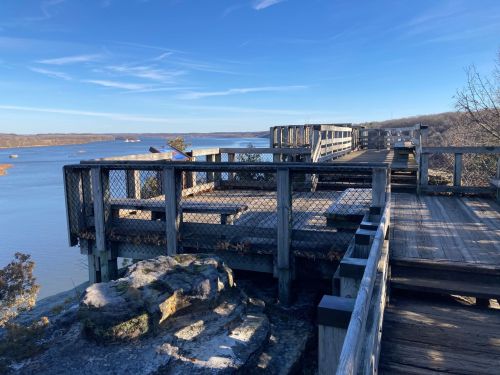 A wooden observation deck overlooking a calm river, surrounded by trees and a clear blue sky.