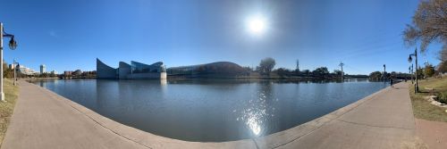 Panoramic view of a calm river with buildings and trees along the shore under a clear blue sky.