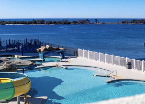 A scenic view of a pool area with a water slide, overlooking a calm body of water and clear blue sky.