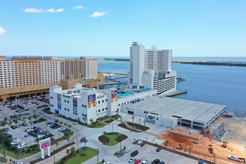 Aerial view of a waterfront hotel complex with a parking lot and construction site, overlooking the water.