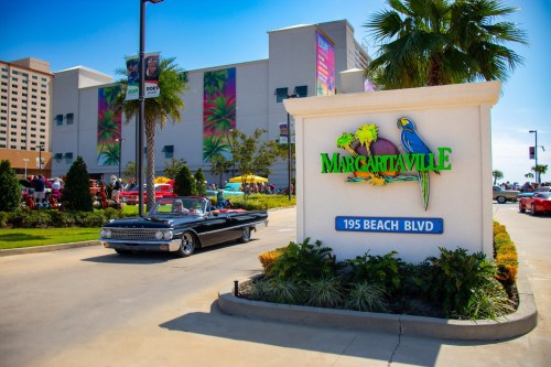 A classic convertible drives past the Margaritaville sign on Beach Blvd, with colorful decorations in the background.