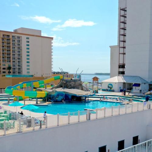 A colorful water slide beside a pool, with people enjoying the area and a view of the water in the background.