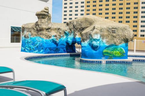A pool area featuring a rock formation with colorful fish murals and lounge chairs nearby.