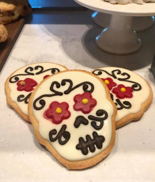 Three decorated sugar cookies shaped like skulls, featuring colorful flowers and intricate designs on a white icing background.