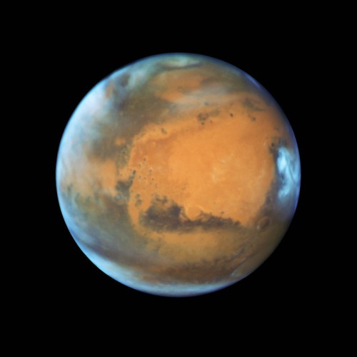 A detailed view of Mars, showcasing its reddish surface and polar ice caps against a black background.