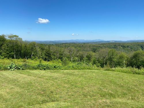 A panoramic view of lush green hills and distant mountains under a clear blue sky with a few clouds.
