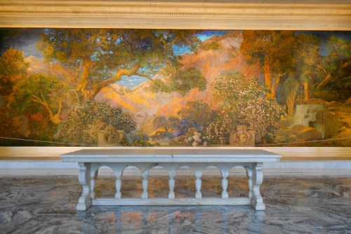 A large mural of trees and mountains behind a white table in a marble-floored room.