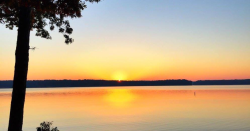 A serene sunset over a calm lake, with vibrant orange and yellow hues reflecting on the water's surface.