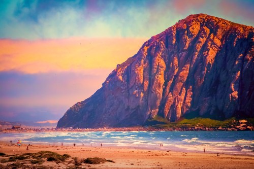 A vibrant beach scene with a towering mountain, colorful sky, and people walking along the shore.