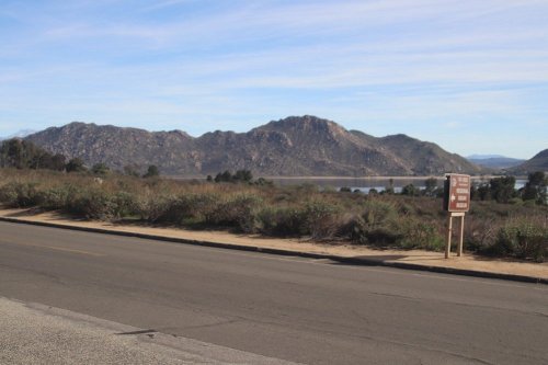 Scenic view of mountains and a lake, with a road and a sign in the foreground. Clear blue sky above.