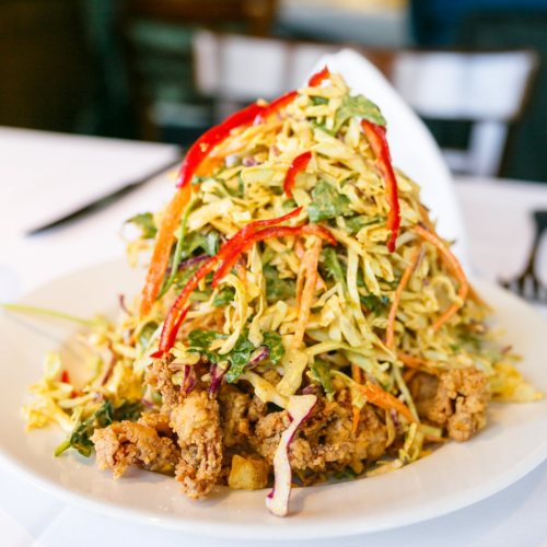 A large plate of crispy fried chicken topped with a colorful, shredded vegetable salad and red pepper strips.