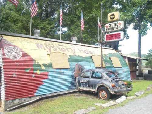 A colorful, weathered building with boarded windows and a rusty car parked outside, surrounded by trees and flags.