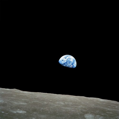Earth rising above the lunar surface, with a dark space backdrop. The moon's gray terrain is visible in the foreground.