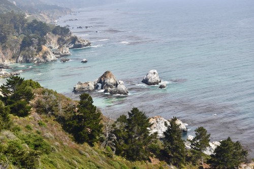 A scenic coastal view featuring rocky formations and lush greenery along the shoreline under a clear sky.