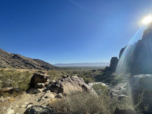 A scenic view of a desert landscape with mountains, clear blue sky, and sunlight shining on rocky formations.