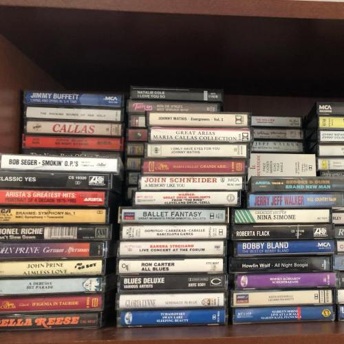 A shelf filled with various cassette tapes, featuring artists like Jimmy Buffett, Bob Seger, and Jerry Jeff Walker.