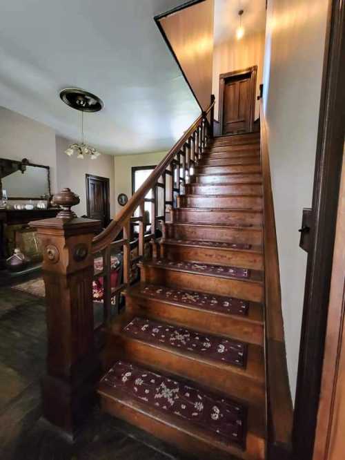 A wooden staircase with a decorative railing, leading to a door at the top, illuminated by a ceiling light.