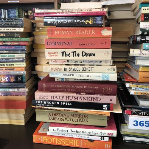 A stack of books on a table, featuring titles by various authors, with colorful spines and varying sizes.