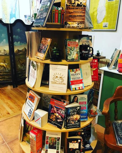 A wooden display shelf filled with various books and a coffee mug in a cozy bookstore setting.