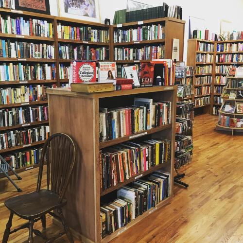 A cozy bookstore interior featuring wooden shelves filled with books and a chair in the foreground.