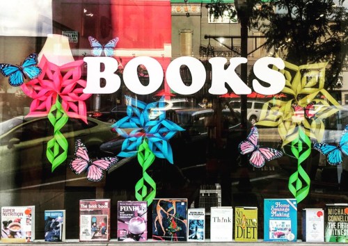 Colorful window display featuring the word "BOOKS" with paper flowers and butterflies, showcasing various magazines below.