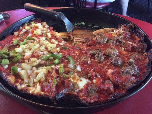 A large pizza with a thick crust, topped with meatballs, green peppers, onions, and pineapple, served in a deep dish.