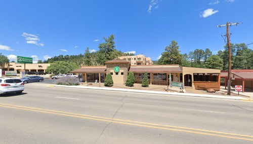 A street view of a single-story building with a sign, surrounded by trees and clear blue skies.