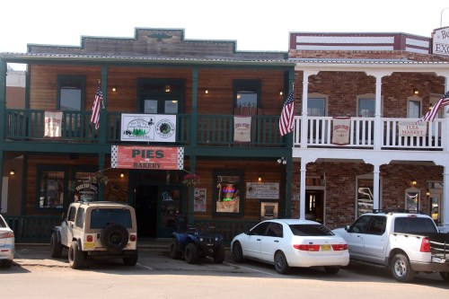 Historic buildings with balconies, featuring a bakery sign and parked vehicles in front, adorned with American flags.
