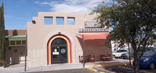 Exterior of a bakery and café with a colorful archway, outdoor seating, and a clear blue sky.