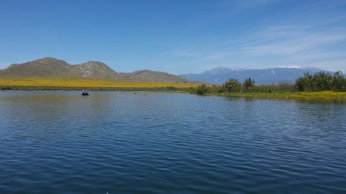 A serene lake surrounded by mountains and lush greenery under a clear blue sky.